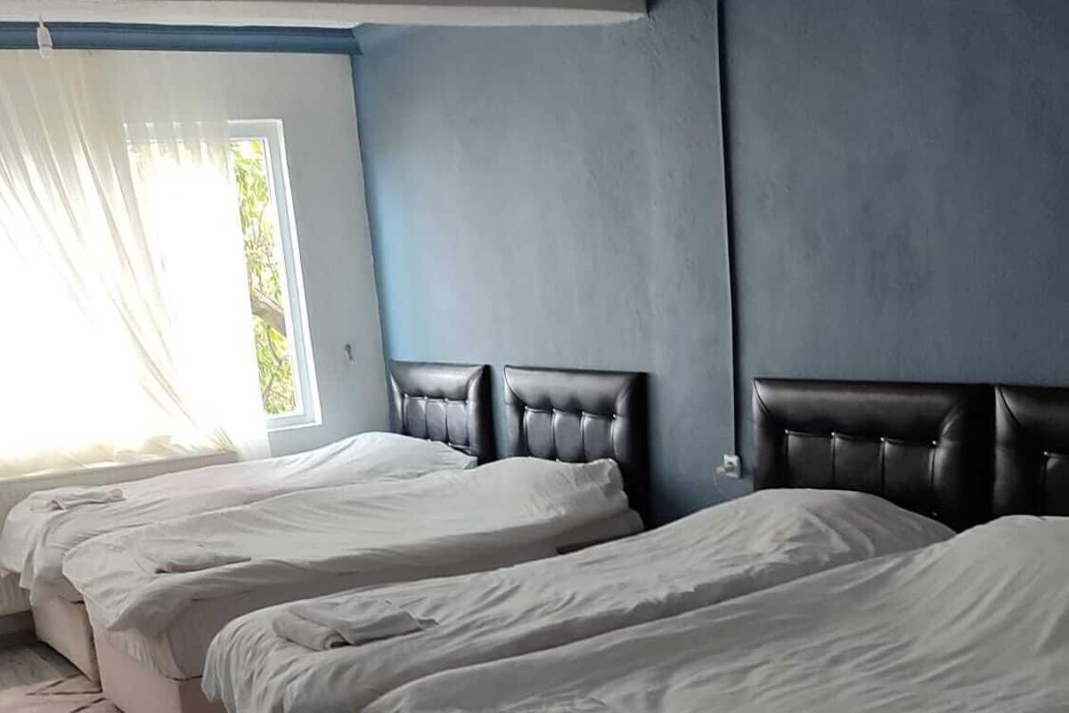 A hotel room with four beds arranged in a row, a large window with curtains, and a blue wall.