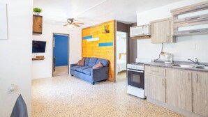 A compact living space with a kitchenette, a sofa, a ceiling fan, and a TV.