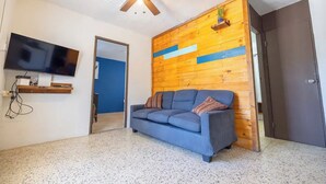 A room with a blue sofa, wooden wall paneling, a ceiling fan, a mounted TV, and a door.