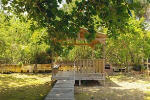 A wooden pergola structure with a wooden deck, surrounded by lush greenery and trees. - Waves & Chill 2 | Jobos Guest House (Isabela)