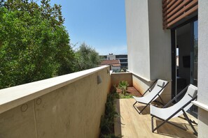 Ein Balkon mit zwei Liegestühlen, einer kleinen Grünfläche und Blick auf benachbarte Gebäude.