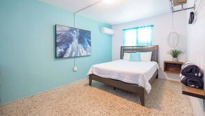 Una camera da letto con un letto, un quadro, una finestra con tende, una pianta e un portasciugamani.