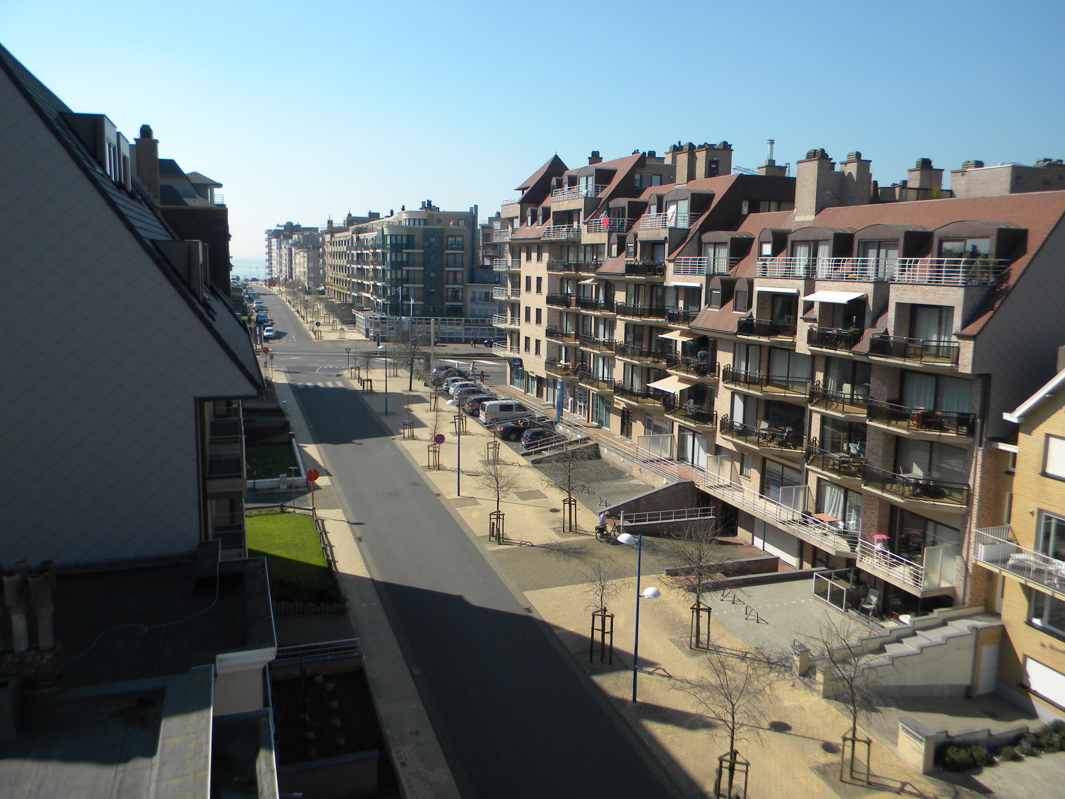 A multi-story residential building with balconies, a parking area, and a clear sky.