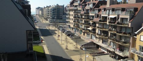 Un edifici residencial de diverses plantes amb balcons, una zona d'aparcament i un cel serè.
