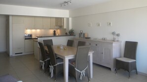 Une cuisine moderne avec des meubles blancs, une table à manger avec des chaises et un petit îlot central doté d’un évier.