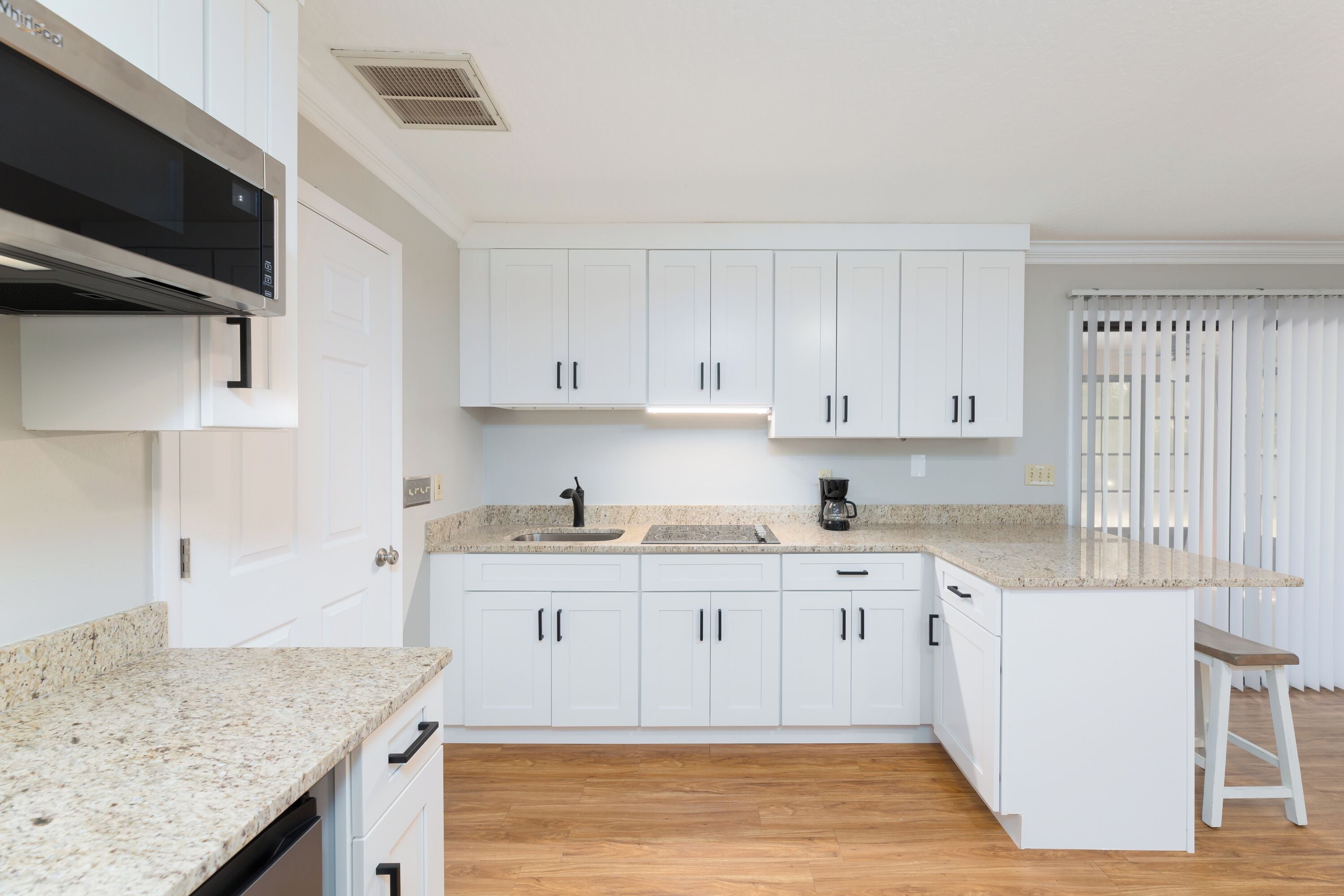 A modern kitchen with white cabinets, granite countertops, a built-in microwave, and a coffee maker.