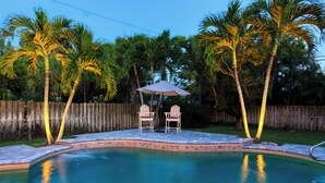 Una piscina con dos sillas Adirondack y un paraguas a rayas.