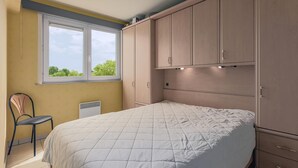 A bedroom with a bed, a chair, a window, and built-in cabinets. - 1 bedroom accommodation in Oostduinkerke (Oostduinkerke)