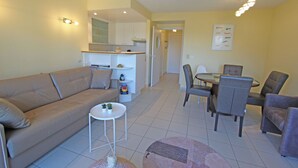 A modern living room with a sofa, a small round table, and a dining area with chairs. - 1 bedroom accommodation in Nieuwpoort (Nieuwpoort)
