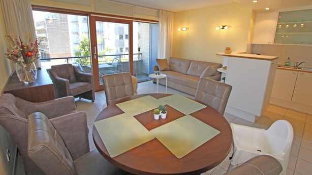 A modern living room with a round table, sofas, and a kitchen area. - 1 bedroom accommodation in Nieuwpoort (Nieuwpoort)