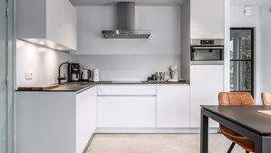 A modern kitchen with white cabinetry, a stainless steel range hood, a built-in oven, and a dining area with a table and chairs. - 2 bedroom accommodation in Oostduinkerke (Oostduinkerke)