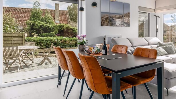 A modern dining area with a large table, orange chairs, and a view of the garden through large windows. - 2 bedroom accommodation in Oostduinkerke (Oostduinkerke)