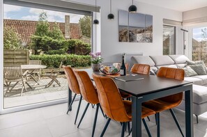 A modern dining area with a large table, orange chairs, and a view of the garden through large windows.