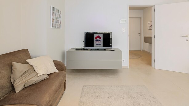 A modern living room with a sofa, a flat-screen TV on a stand, and a door leading to another room. - 2 bedroom accommodation in Oostduinkerke (Oostduinkerke)