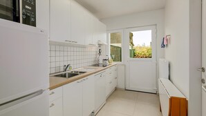 A compact kitchen with white cabinets, a sink, and a window providing a view of greenery outside. - 2 bedroom accommodation in Oostduinkerke (Oostduinkerke)
