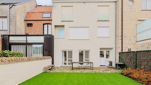 A modern building with a flat roof, a brick facade, and a small garden area with a table and chairs. - 2 bedroom accommodation in Oostduinkerke (Oostduinkerke)