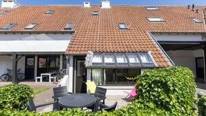 A house with a tiled roof, a covered patio with outdoor furniture, and a bicycle parked outside. - 2 bedroom accommodation in Nieuwpoort (Nieuwpoort)