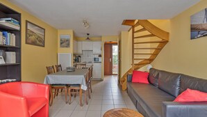 Amplia sala de estar con una mesa de comedor, sillas rojas, un sofá de cuero negro y una escalera de madera.