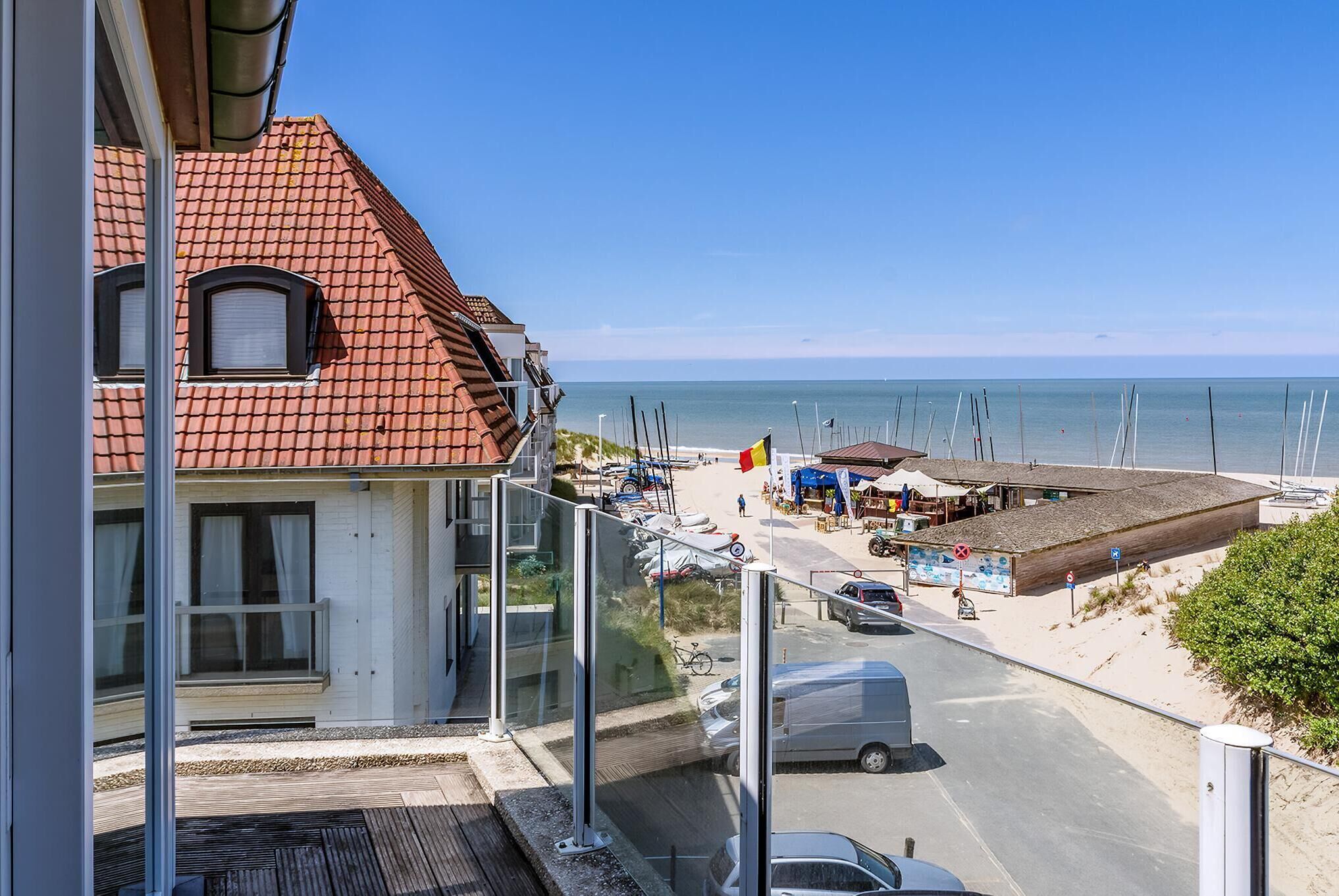 Een kustgebouw met een rood pannendak, een balkon met een glazen balustrade en uitzicht op het strand en de zee.