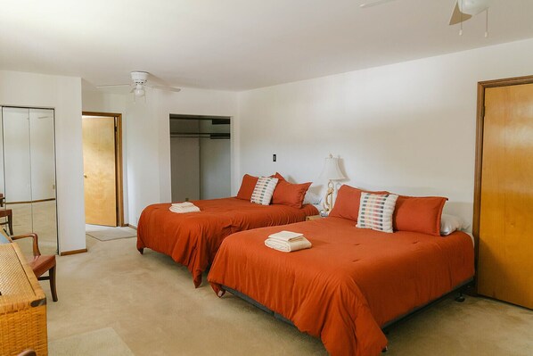 A hotel room with two beds, a ceiling fan, a wooden wardrobe, and a chair.