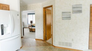 Una cocina compacta con refrigerador, una puerta de madera que da a una sala de estar, y papel tapiz estampado.