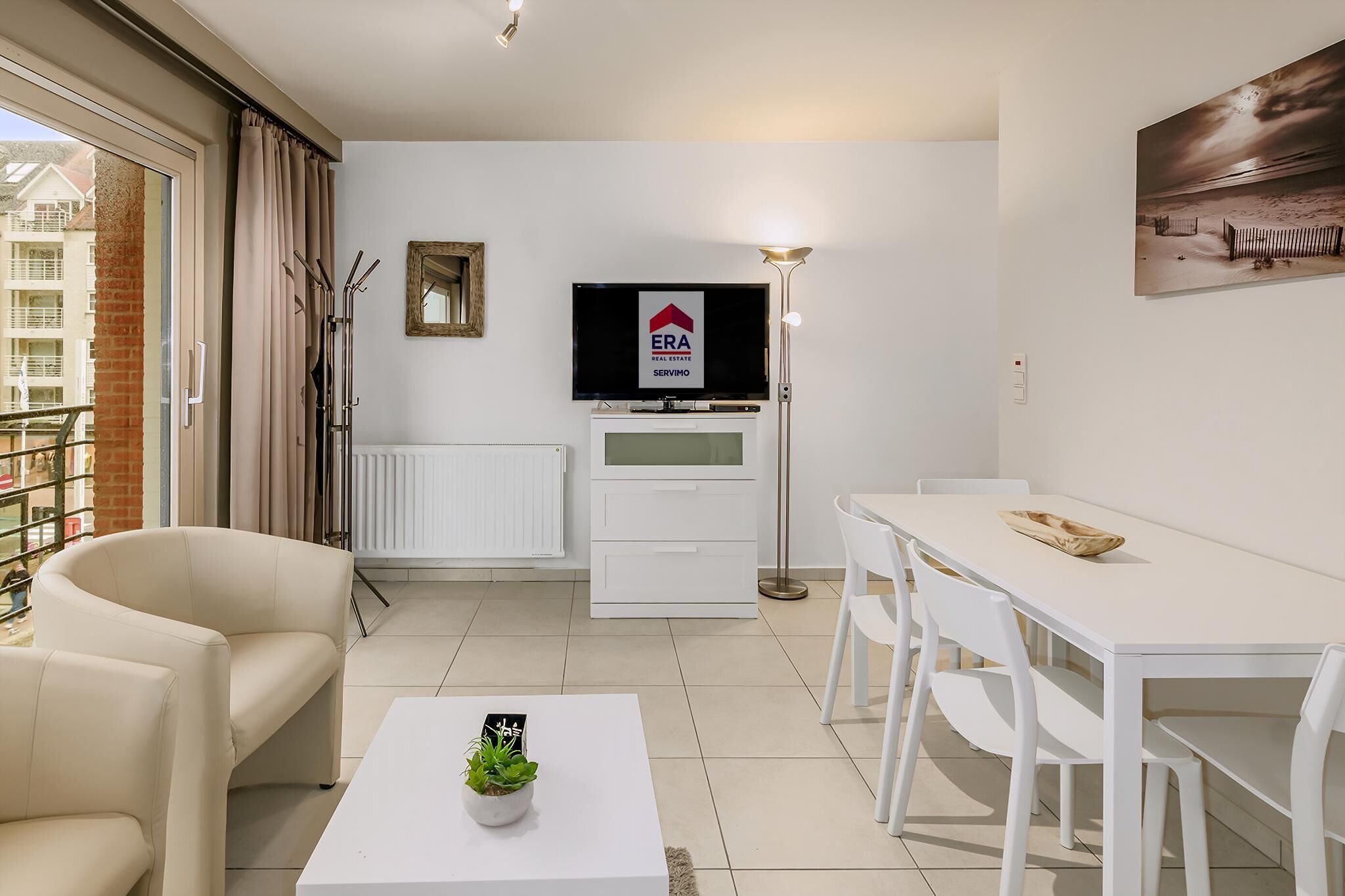 A modern living room with a white sofa, a dining table, and a TV displaying a real estate sign.