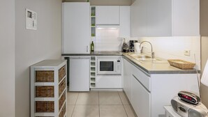 Una cocina compacta con armarios blancos, horno integrado, microondas, pileta y radio.