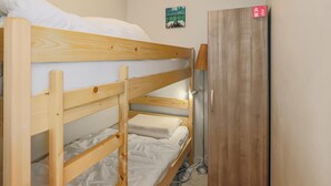 Habitación con literas, un armario de madera y una pequeña estantería mural.