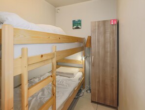 Kerrossängyllä varustettu huone, jossa on puinen vaatekaappi ja pieni seinälle kiinnitetty hylly.