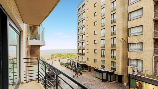 Un edificio de gran altura con múltiples balcones, un espacio comercial en la planta baja y vistas despejadas a la playa.
