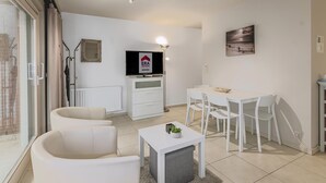 Una sala de estar moderna con un sofá, una mesita con una planta, un televisor y un comedor con sillas.
