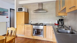 A kitchen with wooden cabinets, a microwave, a stove, and a sink. - 3 bedroom accommodation in Nieuwpoort (Nieuwpoort)