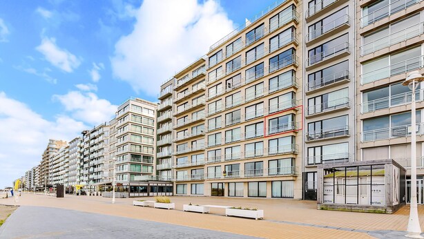 A modern multi-story residential building with balconies, a paved walkway, and a small kiosk.