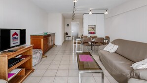 A modern living room with a television, wooden entertainment unit, sofa, coffee table, dining area, and kitchen.