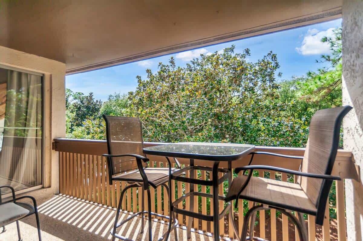 A balcony with a table and chairs, a view of trees, and a wooden railing.