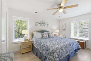 Una camera da letto con un letto, due comodini, una ventola a soffitto e finestre con tende.