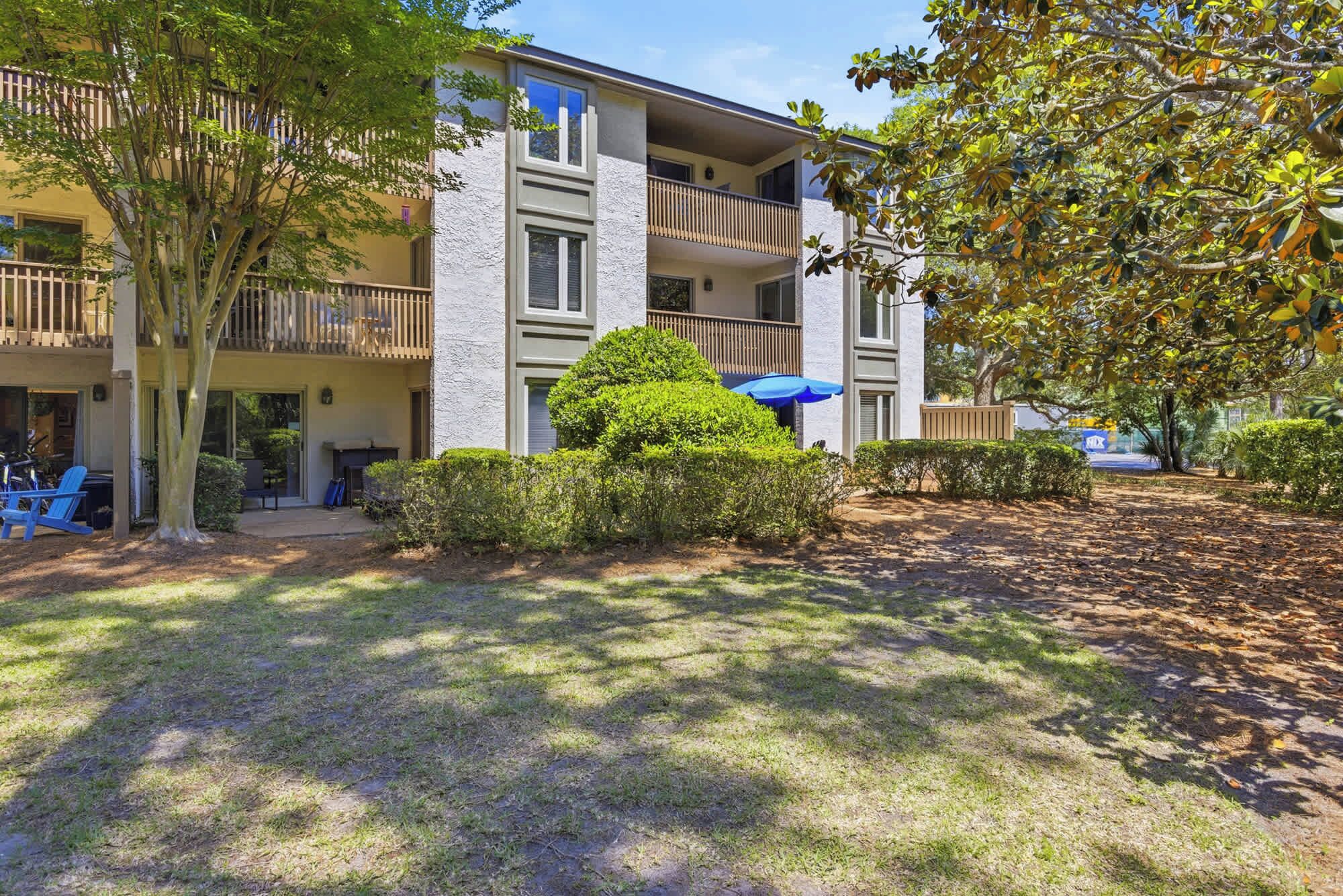 A multi-story building with balconies, a covered outdoor seating area, and a well-maintained lawn.