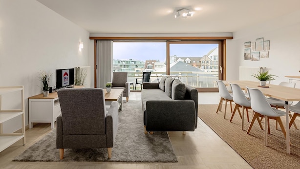 A modern living room with a sofa, chairs, a dining table, and a TV.