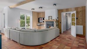 A modern living room with a curved grey sofa, a stone fireplace, and a wooden accent wall. - Villa in Oostduinkerke (Oostduinkerke)