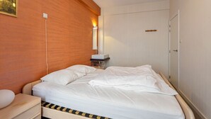 A neatly made bed in a hotel room with a wooden headboard, a bedside table with a lamp, and a wall-mounted light fixture. - 2 bedroom accommodation in Koksijde (Koksijde)