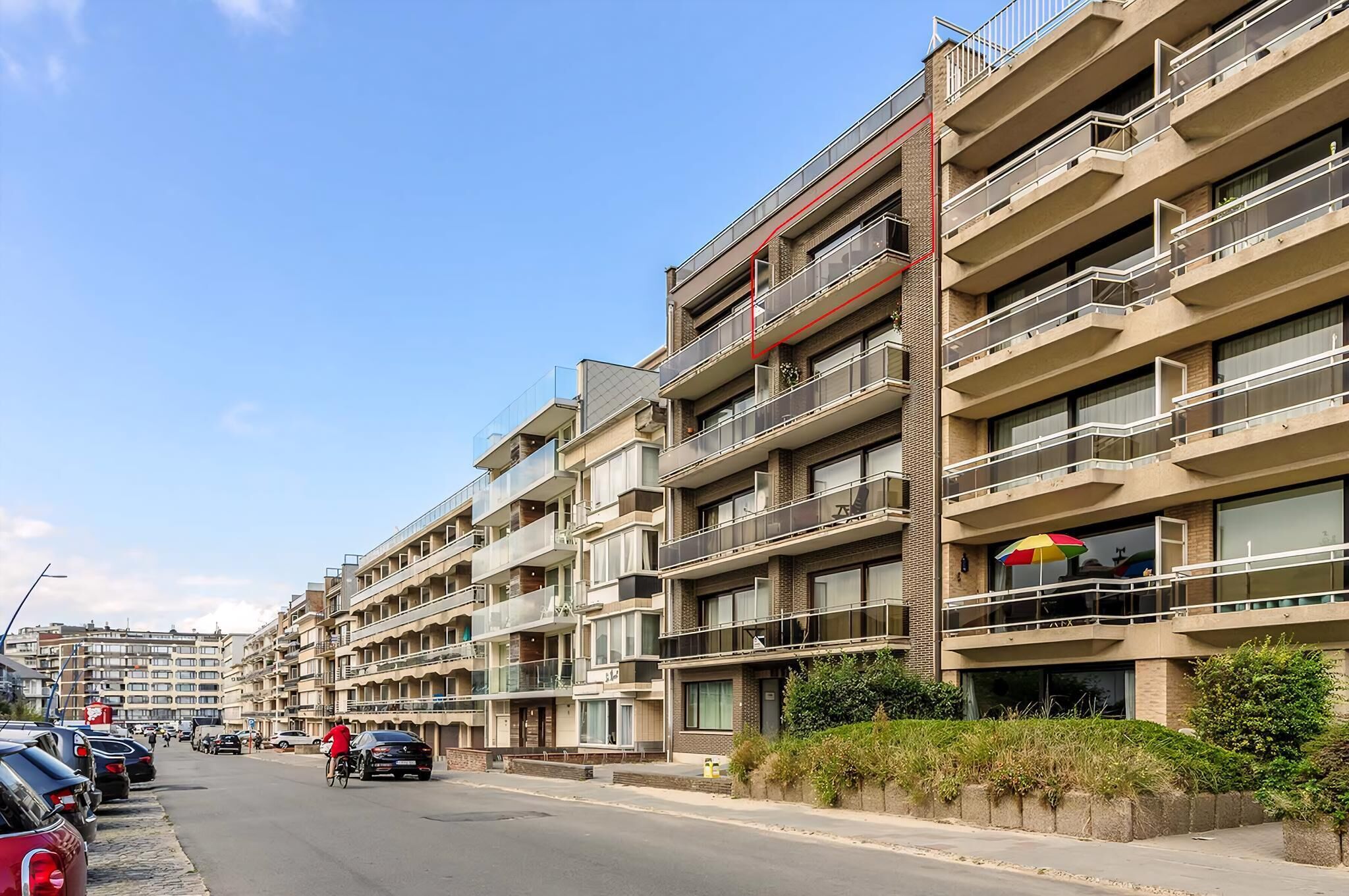 Un immeuble résidentiel à plusieurs étages, doté de balcons, d’un espace de stationnement et surplombant un ciel dégagé.