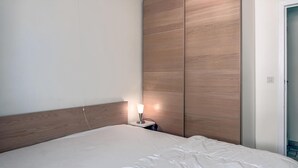 A neatly made bed with a wooden headboard, a bedside lamp, and a wardrobe with a wooden finish.