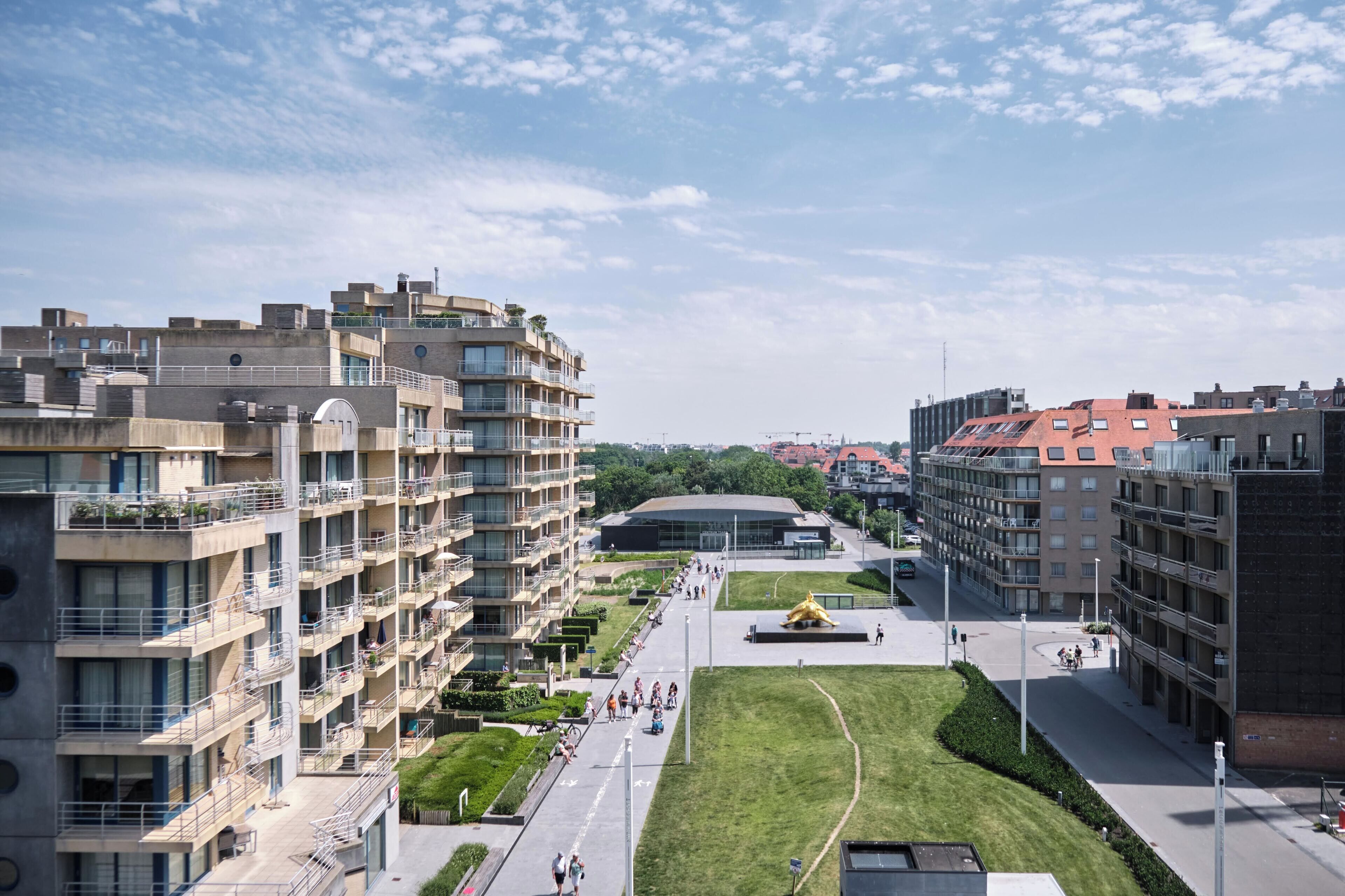 Ein modernes Stadtgebiet mit mehrstöckigen Wohngebäuden, einem zentralen Platz mit einer goldenen Statue und einer großen Kuppel im Hintergrund.