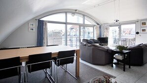 A modern living room with a dining area, large windows, and a view of the city.