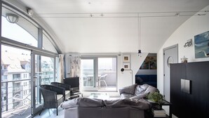 A modern living room with a sofa, a television, and a balcony with a view of the city.