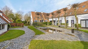 A courtyard with cobblestone paths, a small water feature, and buildings with white walls and red-tiled roofs.