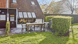 A house with a sloped roof, a wooden table and chairs outside, and a well-maintained garden.