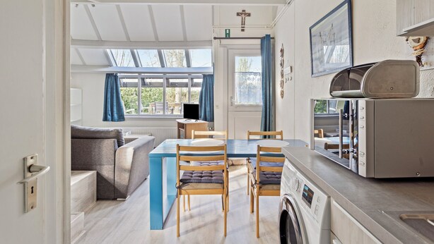 A compact kitchen with a washing machine, a dining area with a table and chairs, and a sofa in the adjacent living space.