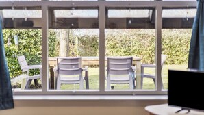 A room with a large window overlooking a garden with a table and chairs.