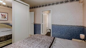 A bedroom with a bed, a wardrobe, a door, and a nightstand with a lamp.